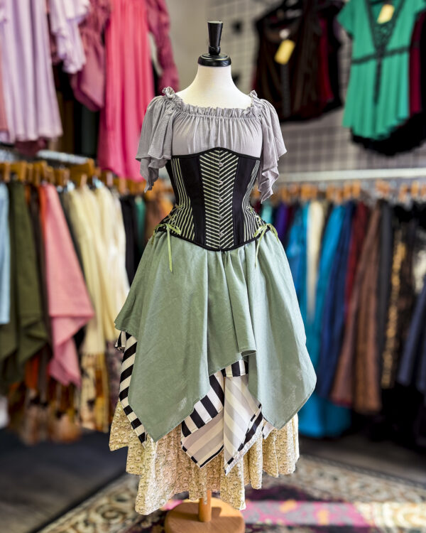 The Eucalyptus Green Linen Pixie Skirt by Faire Treasures displayed in an outfit with greys, blacks, greens, and ivory tones.